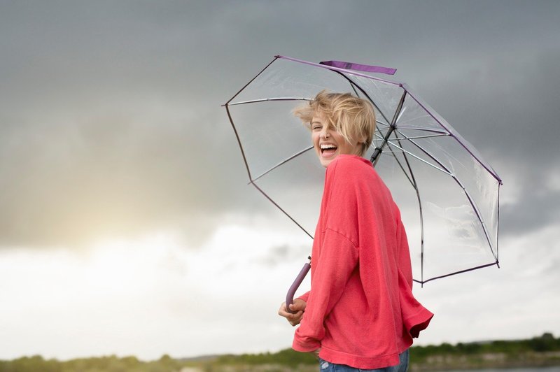 Srečna ženska z dežnikom hodi po dežju. (foto: Profimedia)